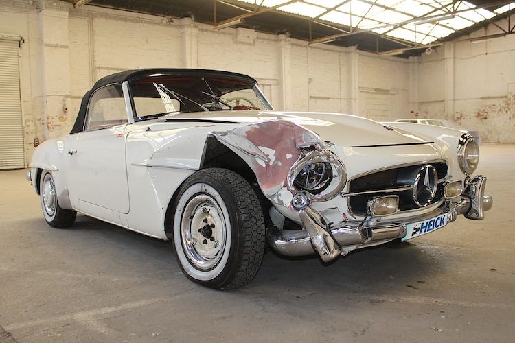 Beschädigter weißer Oldtimer nach einem Unfall in der Halle von einem Unfallgutachter.